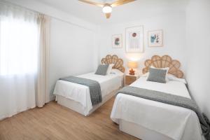 two beds in a bedroom with white walls and wood floors at Marineros Sureste A111 in Torre del Mar