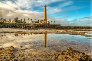 a lighthouse on the beach with its reflection in the water at Casa Margara in Chipiona