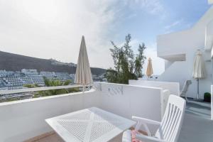 a white balcony with white chairs and an umbrella at Casa Orballo in Mogán