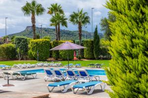 a pool with chairs and an umbrella and palm trees at Apartamento Serendipia in Cala Bona