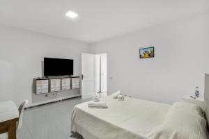 a white bedroom with a bed and a flat screen tv at Casa Mar Azul Arinaga in Arinaga