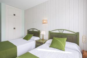two beds in a hotel room with green pillows at Flamingo in Tavernes de Valldigna