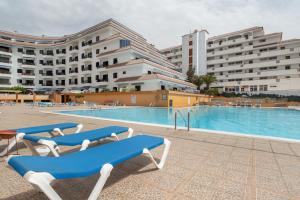 a swimming pool with blue and white chairs and buildings at Apto Jardin del Sol Beach-Pool in Puerto de Santiago