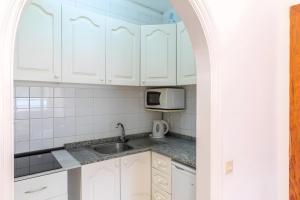 a kitchen with white cabinets and a sink and a microwave at Costamar Oceanview 1 Bed Apartment in Arona