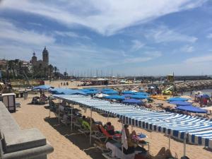 a beach with blue umbrellas and people on the sand at Sitges Llum House in Sitges