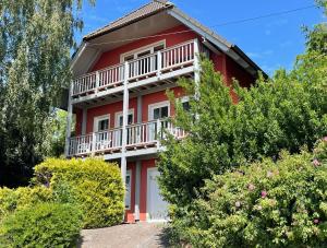 a red house with a balcony and bushes at Küstenblau - Fulgenhaus in Klein Bollhagen