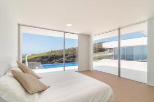 a bedroom with a large white bed and large windows at Villa Camacho - Ultra Luxury in Calheta