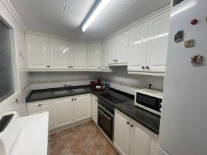 a white kitchen with white cabinets and black counter tops at Nereidas Beachfront in Cullera