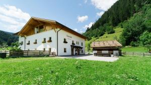 a large white building with a wooden roof and a grass field at Leitnerhof in Racines