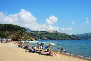a group of people sitting on a beach with umbrellas at App Casa Dei Pini - Bilocale in Capoliveri +4 photos