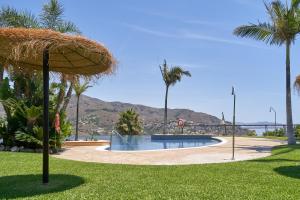 a swimming pool with a straw umbrella and palm trees at Casa Fuentes 2 B2 in Almuñécar