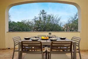 a dining room table with chairs and a large window at Trilo La Rosa in Monte Petrosu