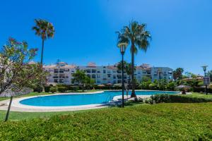 a swimming pool with palm trees and a building at Marbella Beach San Pedro in Marbella