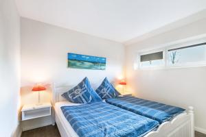 a bedroom with a bed with blue sheets and two windows at Solarferienhaus Wolkenlos in Breklum