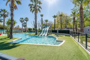 a slide in a swimming pool with palm trees at Mobilhomelaco34 in Vendres