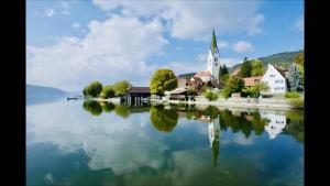 a church on the shore of a lake with its reflection in the water at Gästehaus Bettina in Sipplingen