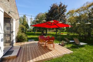 a wooden deck with a table with a red umbrella at Gite La Grange Hulotte in Chaillé-les-Marais