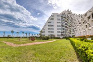 a large white building with palm trees in the background at Le Cosy à la grande pyramide in La Grande Motte