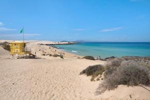 a beach with a yellow house and people on the beach at Falco 1 in Corralejo