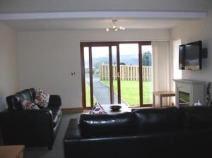 sala de estar con sofá de cuero negro y chimenea en Ty Talcen, en Pennal