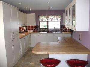 a kitchen with white cabinets and red chairs in it at Ty Talcen in Pennal