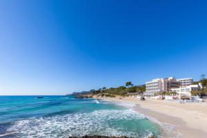 a beach with buildings and the ocean on a sunny day at Bona Mar in Cala Ratjada