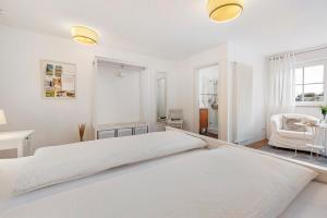 a white bedroom with two beds and a chair at Privatzimmer Kippenhausen in Immenstaad am Bodensee