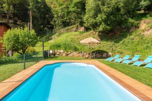 a blue swimming pool with chairs and an umbrella at Ca la Montse in Viladrau