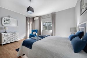 a white bedroom with a large bed and blue chairs at Casa Vista Rio in Ferragudo