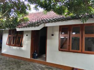 a small white house with wooden windows and a tree at Sekar Homestay in Bantul