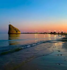 a sunset on the beach with a rock in the water at Villetta Nicola in Salve