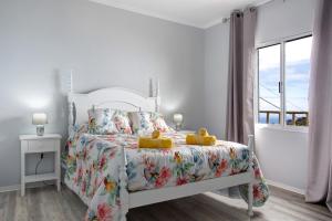 a white bedroom with a bed with a floral bedspread at Casa da Ribeira da Janela in Porto Moniz