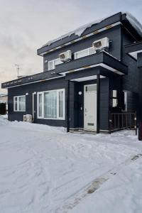 a black house with a white door in the snow at Furano Noie in Furano