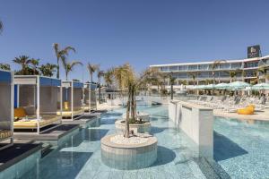 a swimming pool with chairs and trees and a building at Faros Hotel Ayia Napa in Ayia Napa