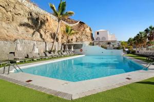 a large swimming pool with chairs and a mountain at Apartamento Joya in Puerto Rico de Gran Canaria