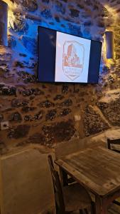a television hanging on a stone wall with a wooden table at Pyrgos Mitsakou 2 in Vathia