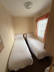 two beds in a small room with a window at Sunnymede G20 with Hot Tub - pet friendly, Wifi, bed linen - Meadow Lakes Caravan & Lodge Hire in Ingoldmells