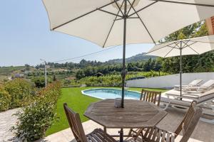a wooden table and chairs with an umbrella and a pool at Refugio Das Vinhas in Celorico de Basto