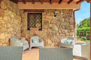 a patio with white chairs and a stone wall at Dependance con piscina in Punta Molara