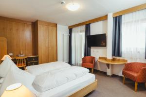 a hotel room with a white bed and a table and chairs at Hotel Tyrol in Funes