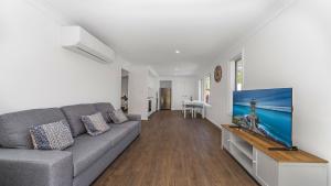 a living room with a gray couch and a tv at 'Coastal Harmony Cottage' by HolidayCo in Hardys Bay