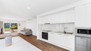 a kitchen with white appliances and a living room at 'Coastal Harmony Cottage' by HolidayCo in Hardys Bay