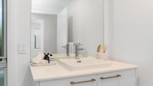 a white bathroom with a sink and a mirror at 'Coastal Harmony Cottage' by HolidayCo in Hardys Bay +3 photos