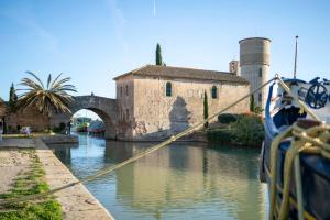 a boat is docked in a canal with a building at Le Somail - Louis 14 in Ginestas