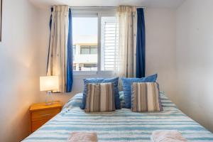 a bed with blue pillows in a bedroom with a window at Apartamento Trilo 24 in Es Pujols