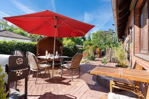a patio with a table and a red umbrella and a bench at Ferienhaus Ankerglück in Lensahn
