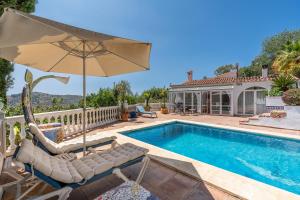 a pool with chairs and an umbrella next to a house at Villa Villena Torrox in Torrox