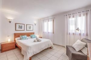 a white bedroom with a bed and a chair at Mariners in Alcudia