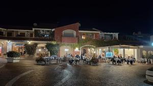 a group of people sitting at tables in a courtyard at night at Apartments Porto Ottiolu Mare in Porto Ottiolu