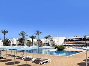 a swimming pool with chairs and umbrellas next to a resort at Residencial Primavera in Arona